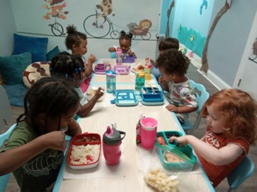 Children enjoying mealtime at a daycare near Darien, CT, sitting around a table with lunchboxes.