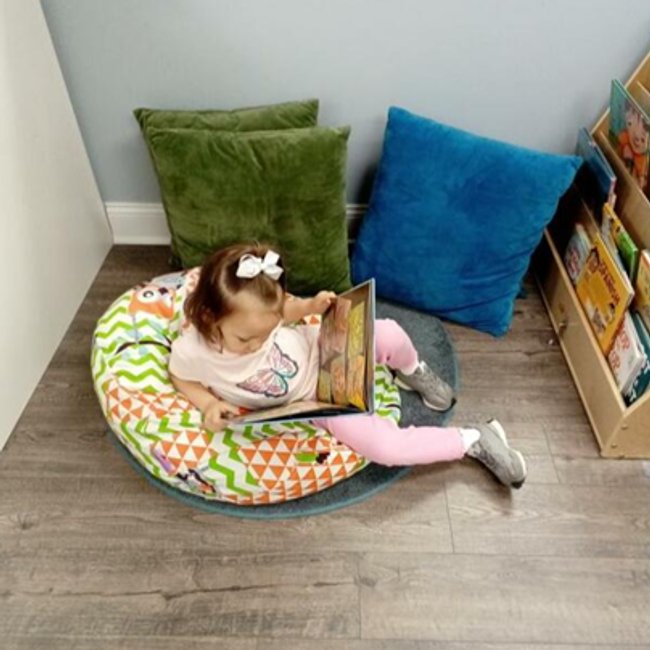 Child reading at daycare in Glenbrook CT with colorful cushions and books.