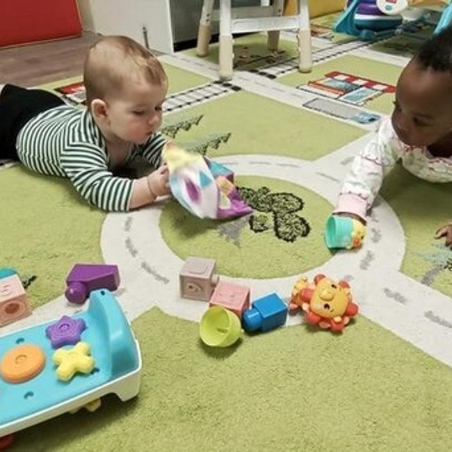 Infants playing at a daycare near Darien, CT with toys on a play mat.