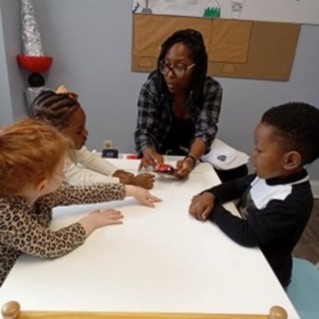 Teacher engaging with pre-k children at a table in Darien CT classroom, focusing on kindergarten readiness.